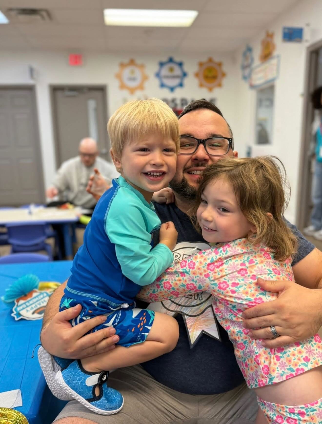 A dad hugging two smiling children during a school family event